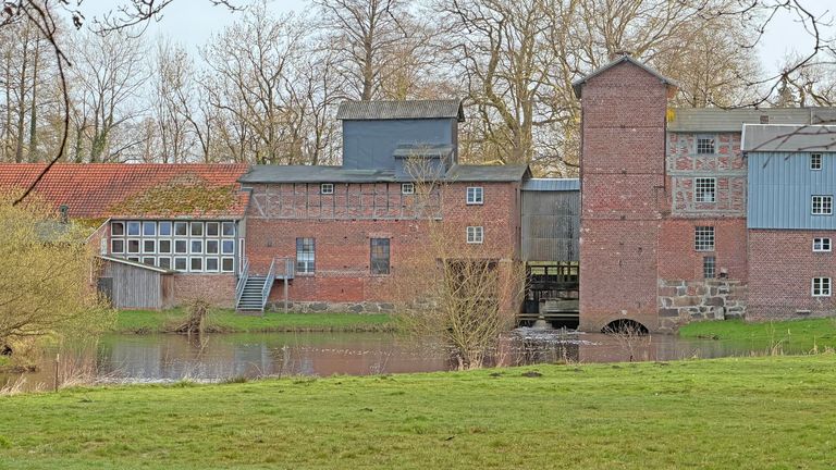 Alte Industriegebäude mit verfallenen Backsteinmauern und Wasserfläche im Vordergrund.